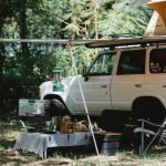 offroader with awning and tent on roof placed in green forest