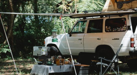 offroader with awning and tent on roof placed in green forest