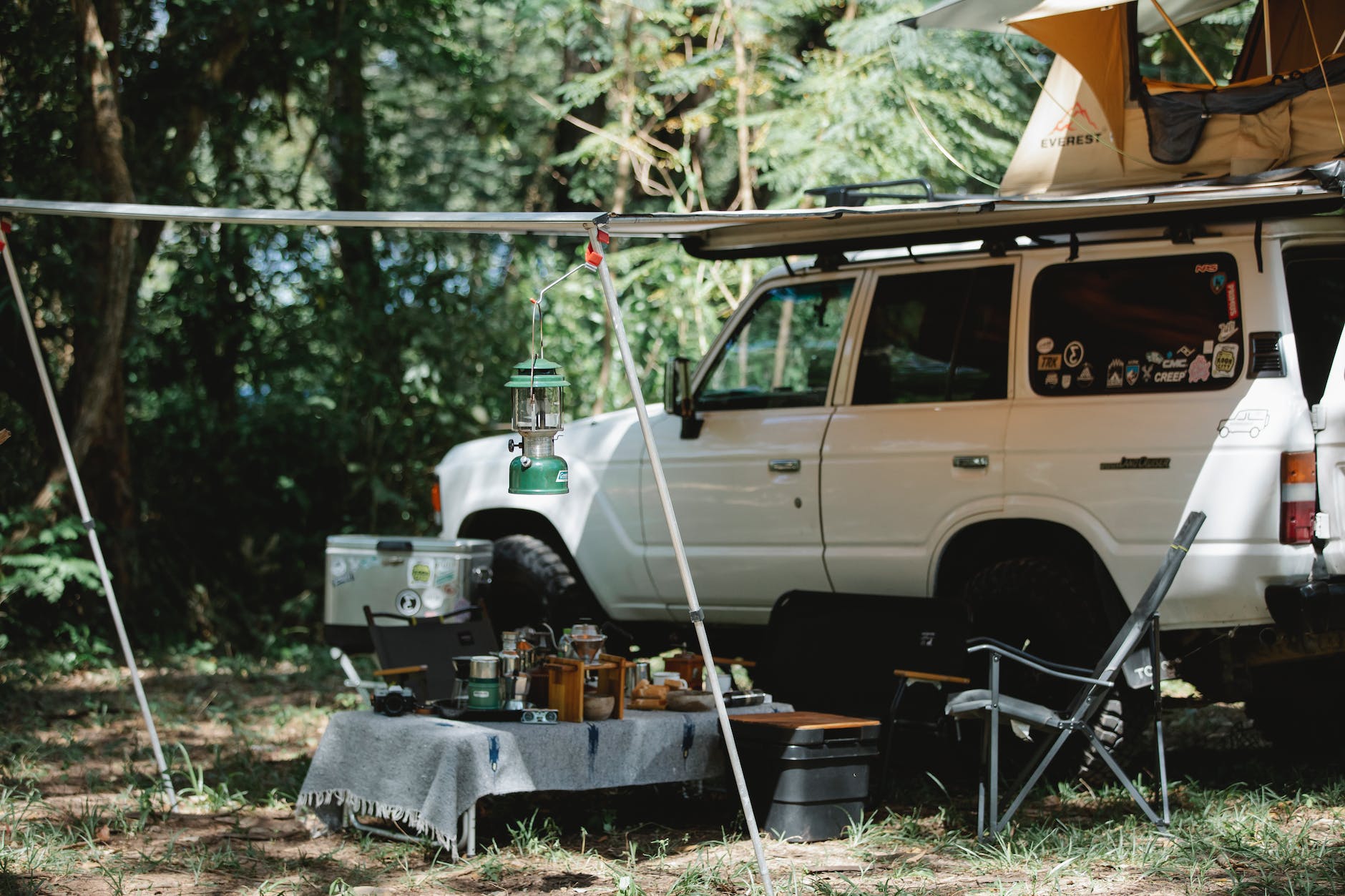 offroader with awning and tent on roof placed in green forest