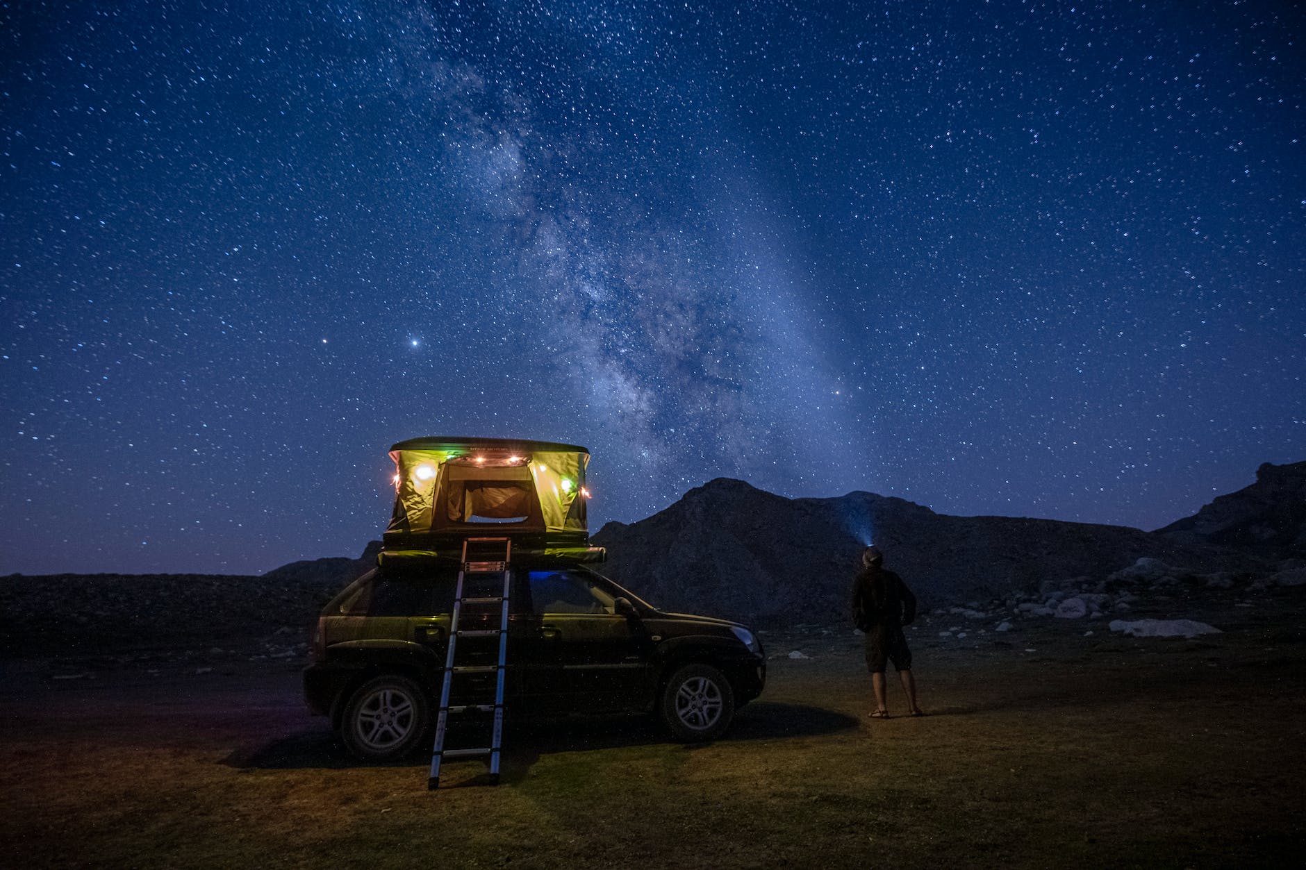 a back view of a person standing near the camper van under the starry sky